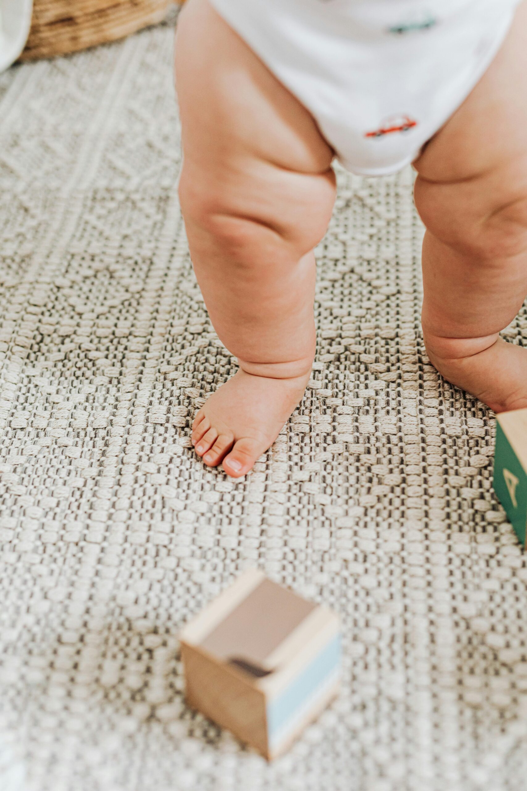 Candid shot of a baby's legs standing on carpet with toy blocks scattered around.